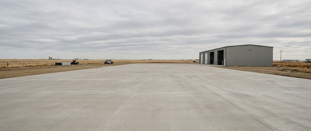 Finished concrete apron in front of a grey steel industrial building under an overcast prairie sky